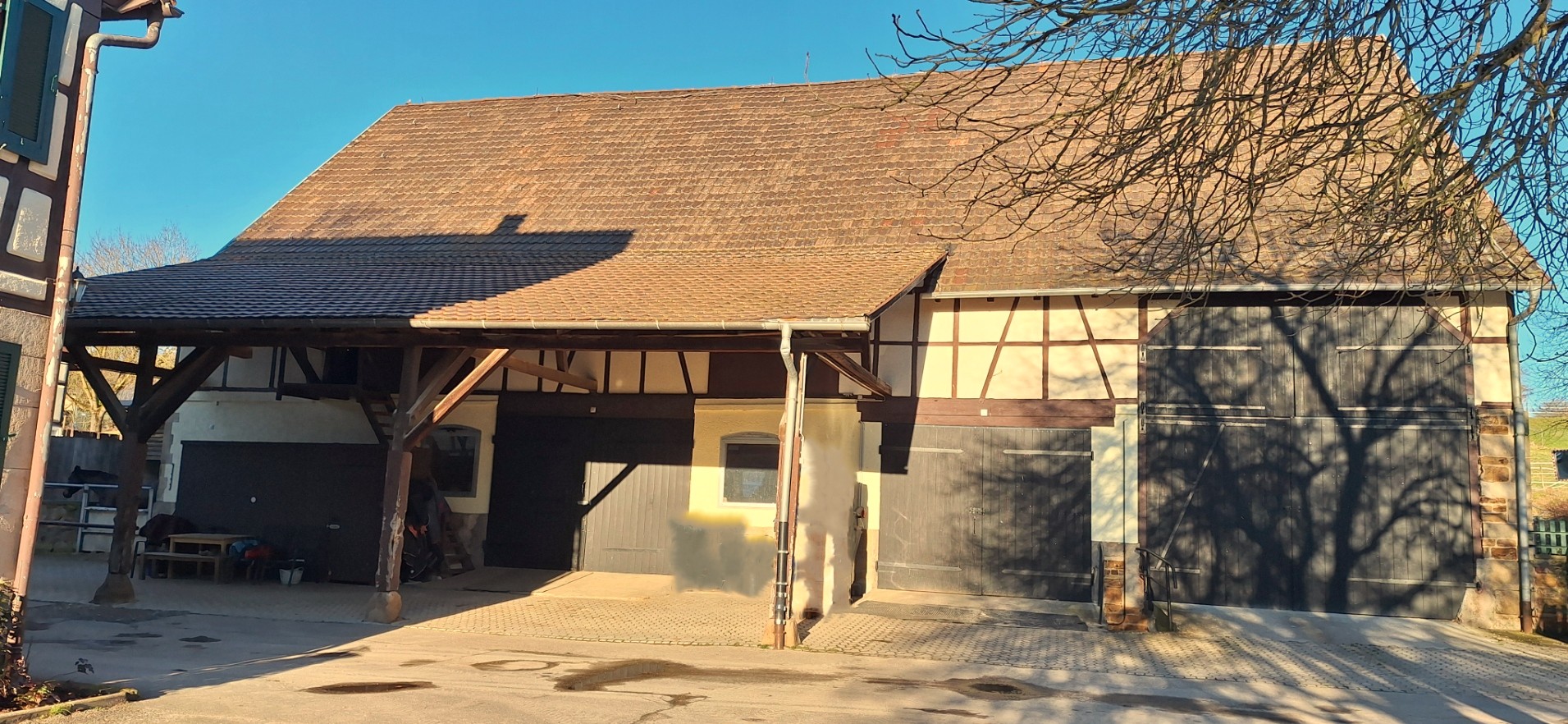 Große Fachwerkscheune mit Satteldach und vorgezogenem Vordach auf Holzpfeilern, aufgenommen bei tiefem Sonnenstand im Spätherbst