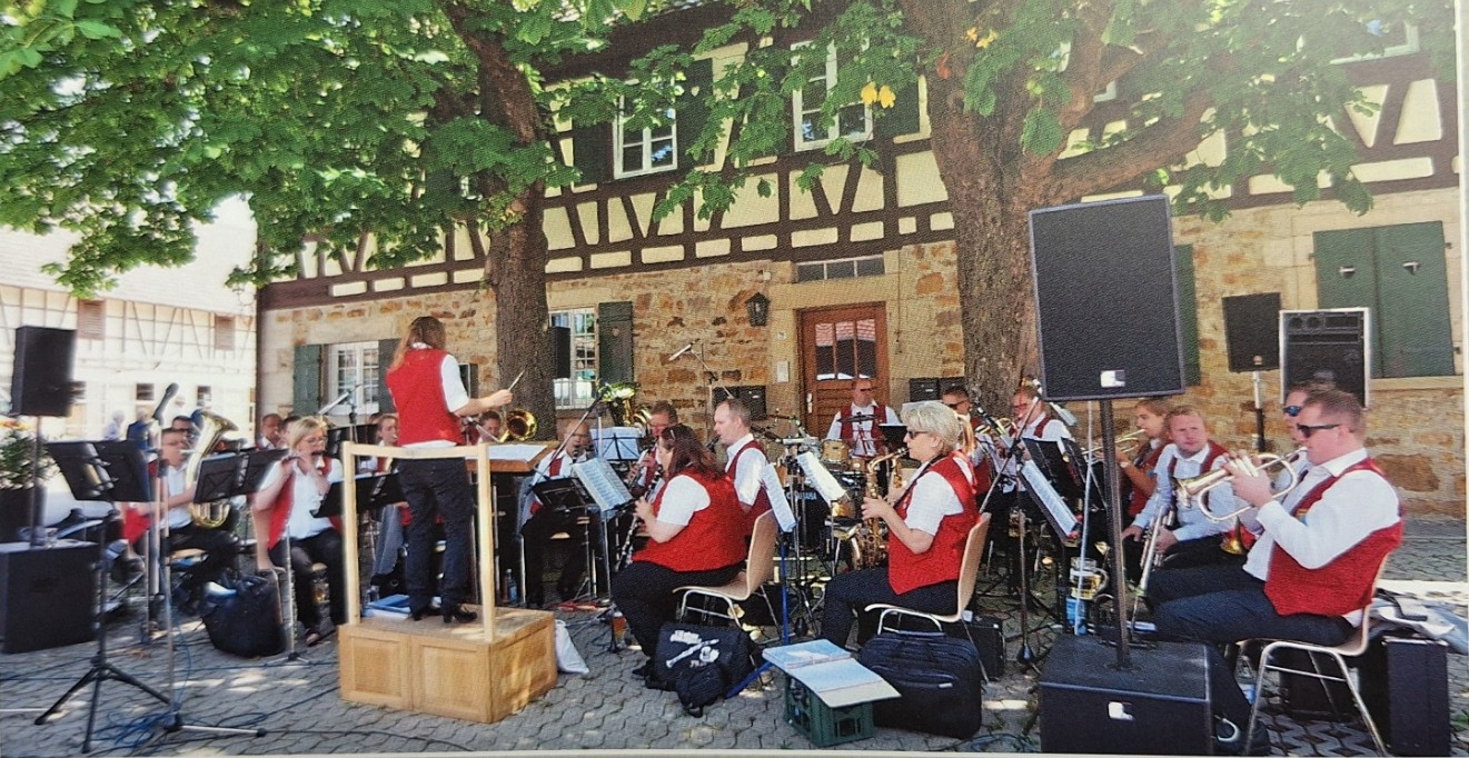 Blasorchester in roten Westen spielt auf dem gepflasterten Platz unter Bäumen