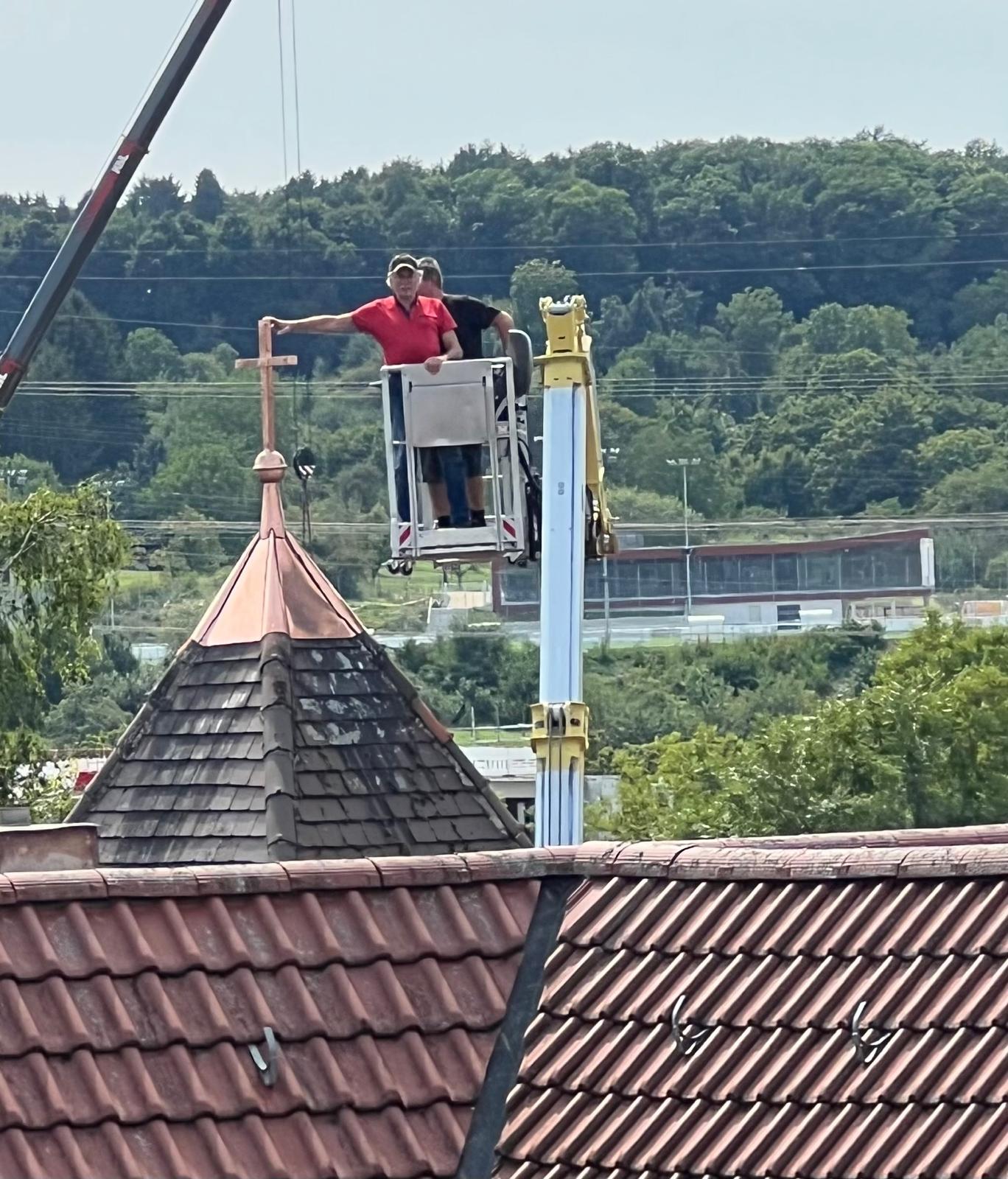 Zwei Männer im Korb einer Hebebühne montieren das kupferne Kreuz auf der Turmspitze der Jakobskirche