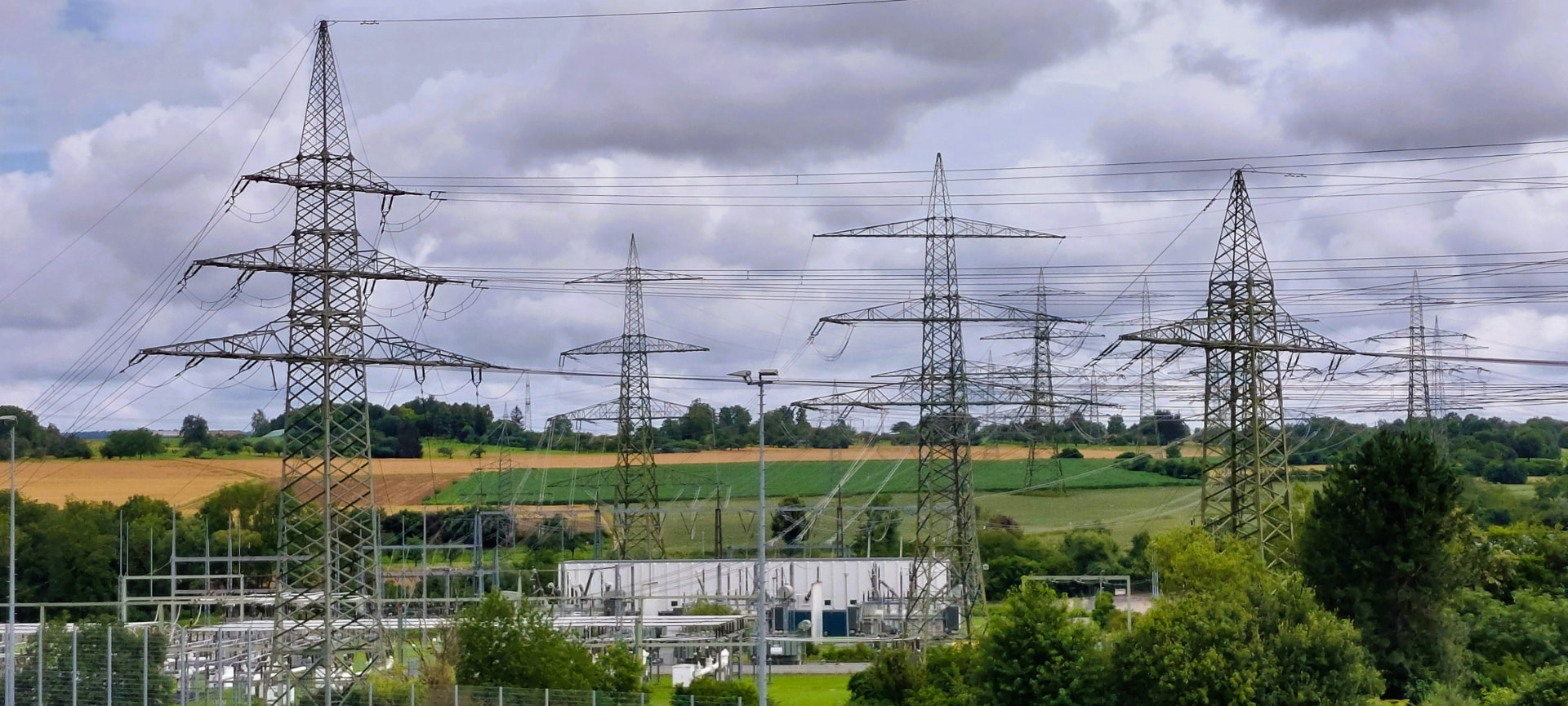 Umspannwerk und hohe Strommasten mit Hochspannungsleitungen vor hügeligen Feldern